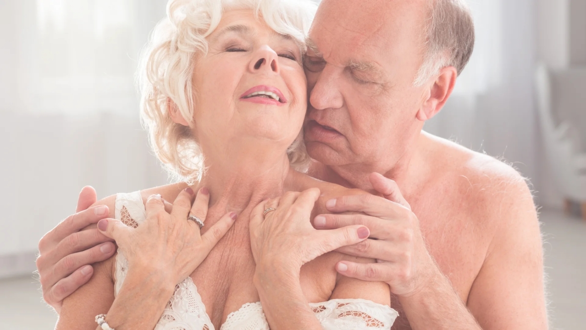 An older couple close together, the woman in white lace and the man's hands on her shoulders