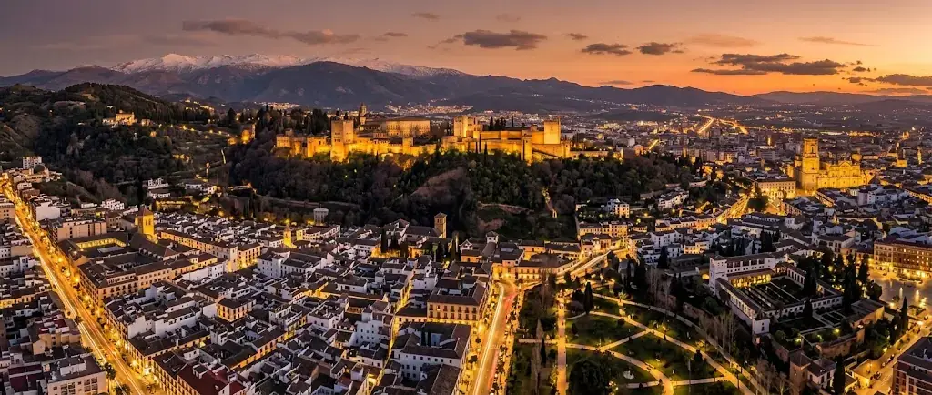 Vista aérea de Granada al atardecer, con la Alhambra iluminada y Sierra Nevada nevada al fondo
