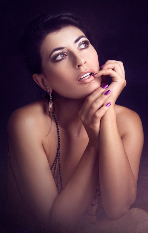 Illustrative stock photo of a close portrait of a woman touching her lip against a dark background. Does not depict a real member.