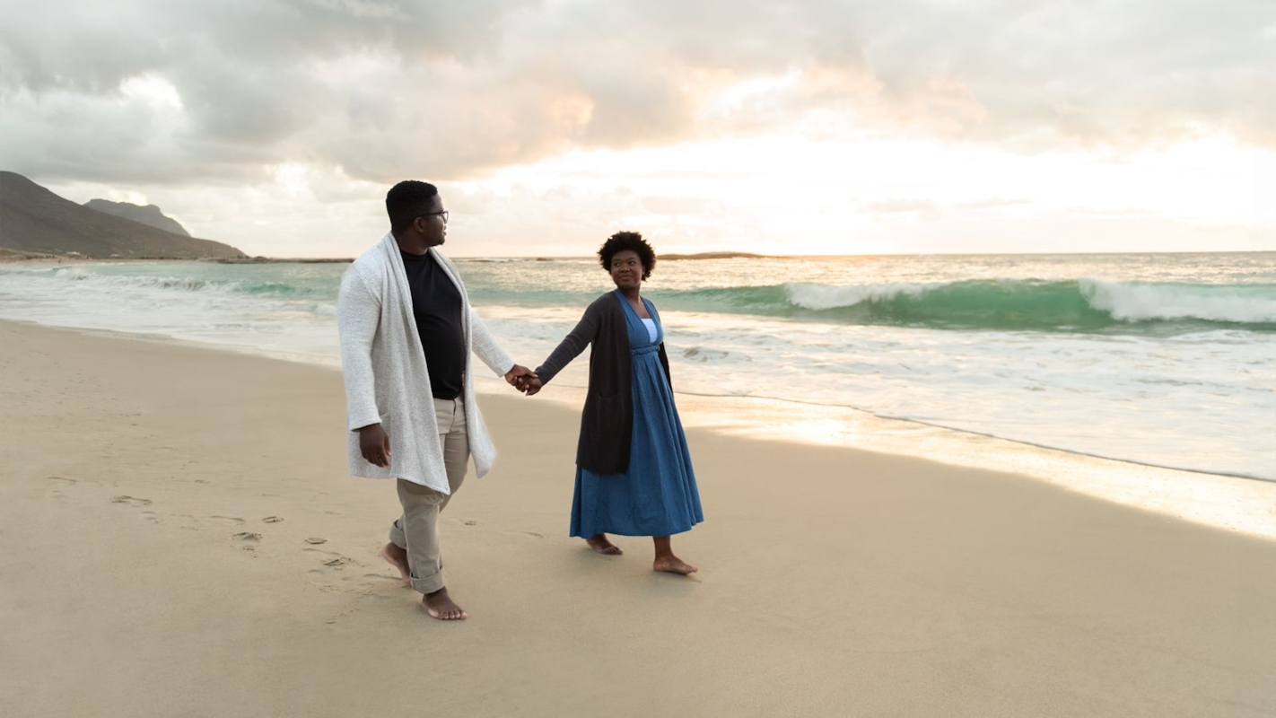 A couple holding hands and walking along the beach at sunset