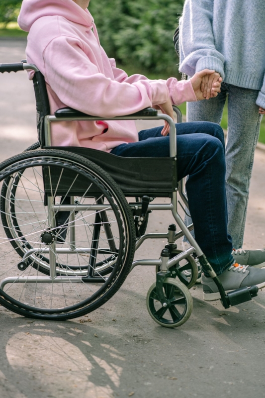 Close-up of a man in a wheelchair holding hands with a companion walking beside him