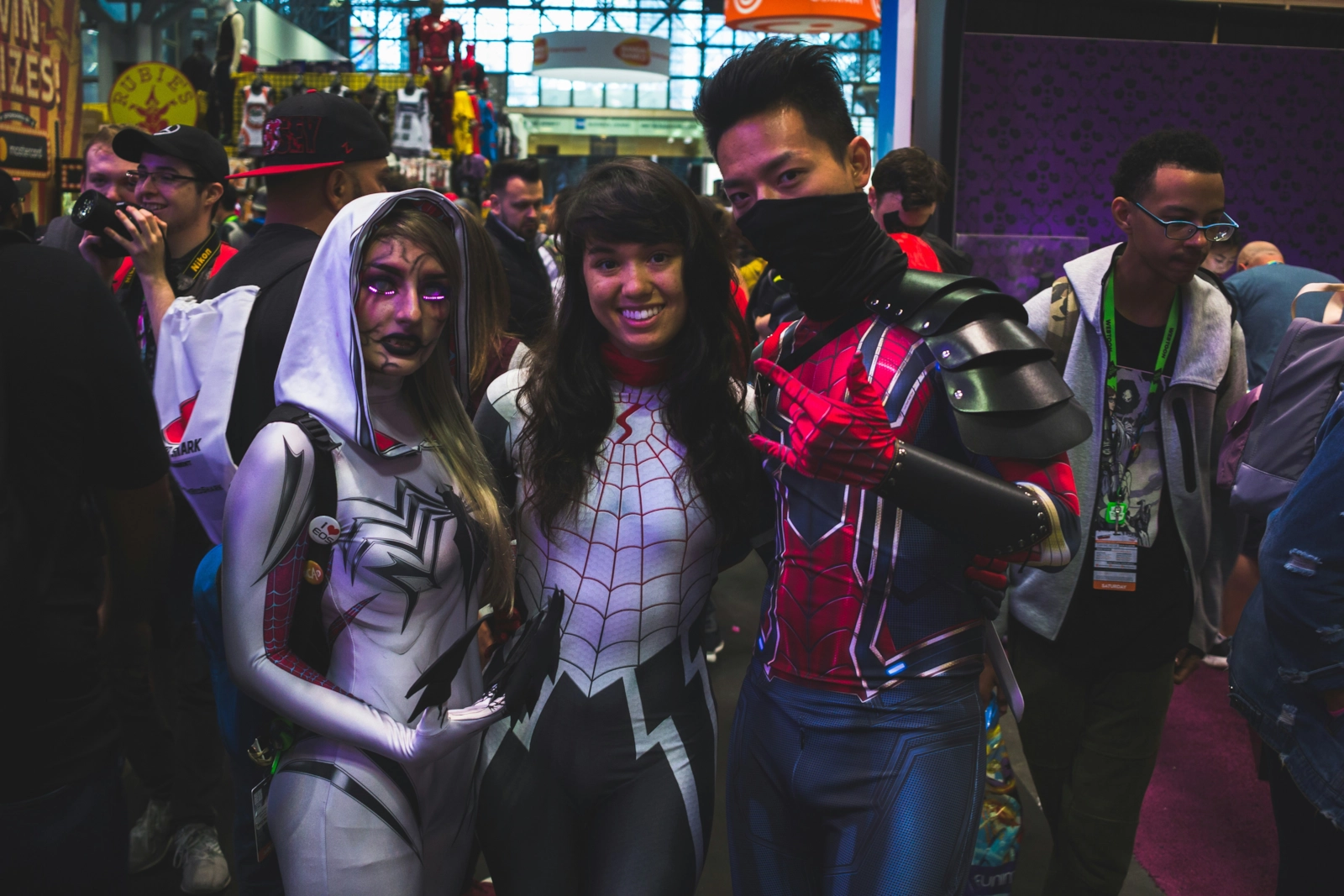 Three fans in Spider-themed costumes posing together at a convention