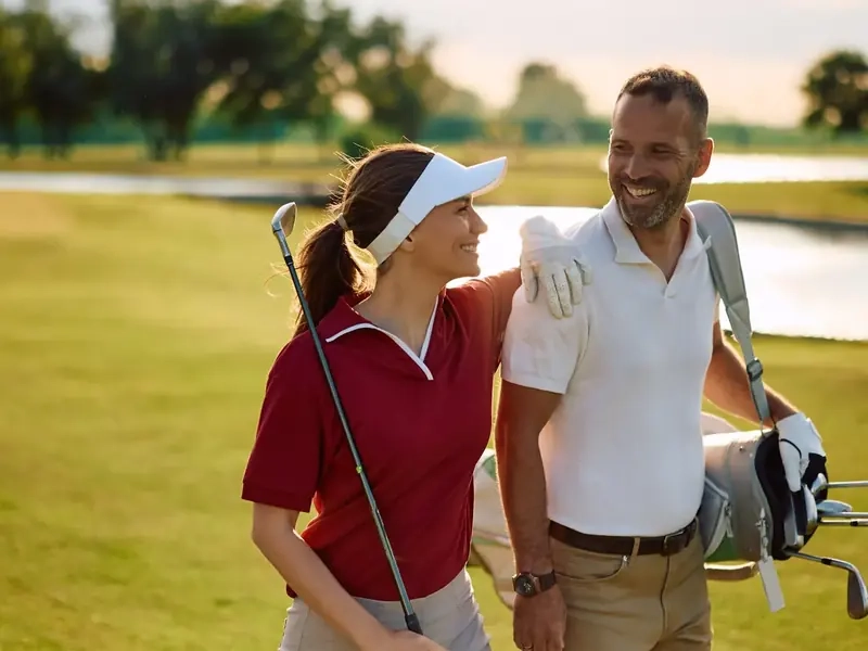 A smiling couple in their forties walking a sunny golf course with a bag of clubs