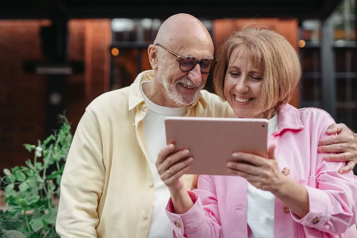A laughing couple looking at a tablet together outside a brick house