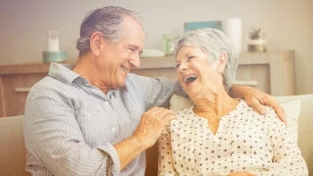 An older couple sharing a laugh on a sofa at home