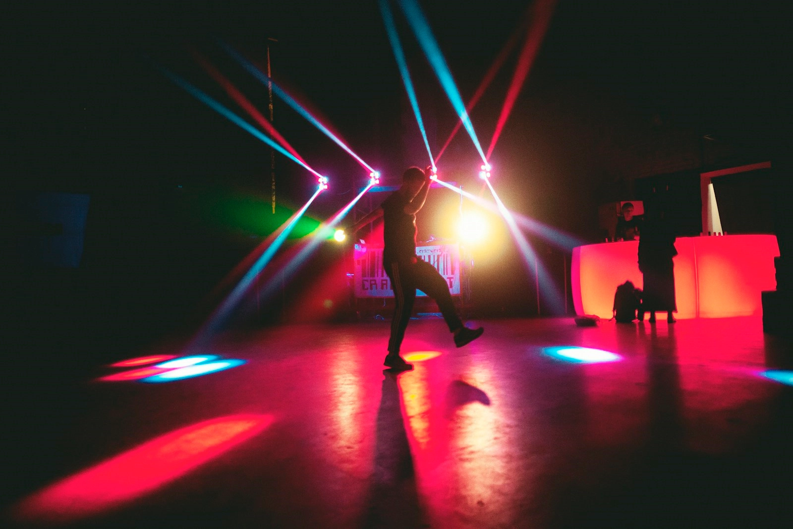 A lone dancer under laser beams on an empty dancefloor