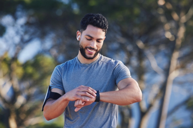 A smiling man in running gear checking his sports watch