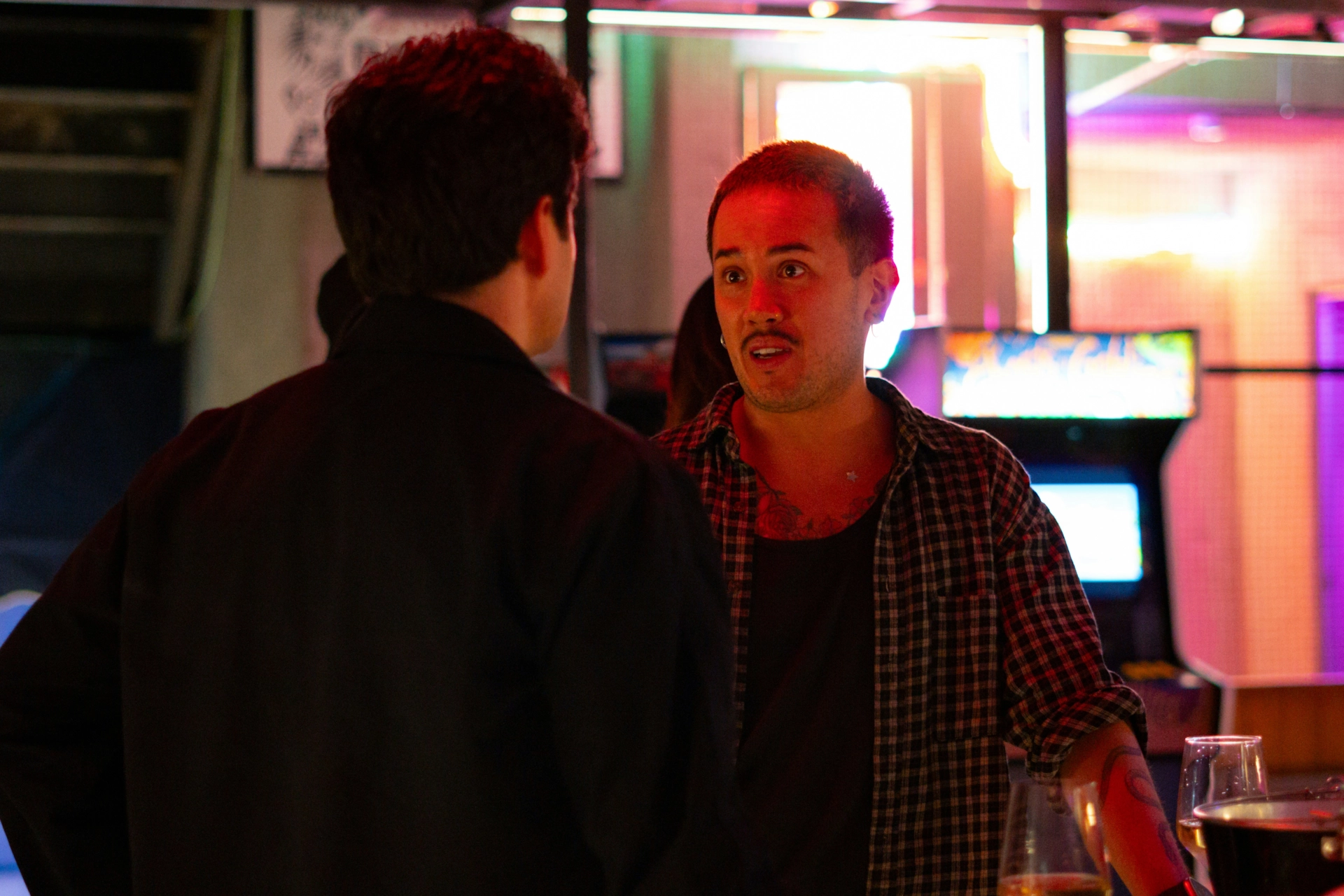 Dos hombres conversando en un bar iluminado con neones.