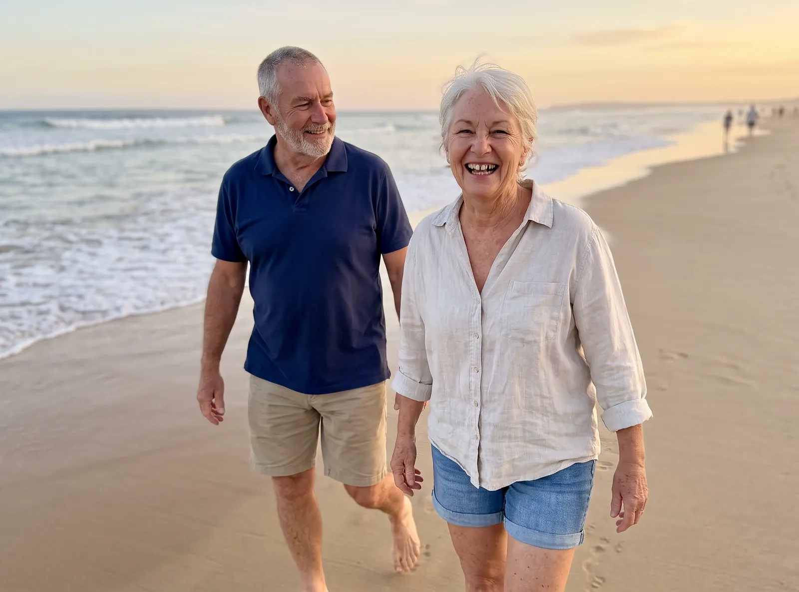 A sun-tanned couple in their sixties walk barefoot along a wide beach at golden hour, she in a linen shirt, he in a navy polo shirt (AI-generated image)