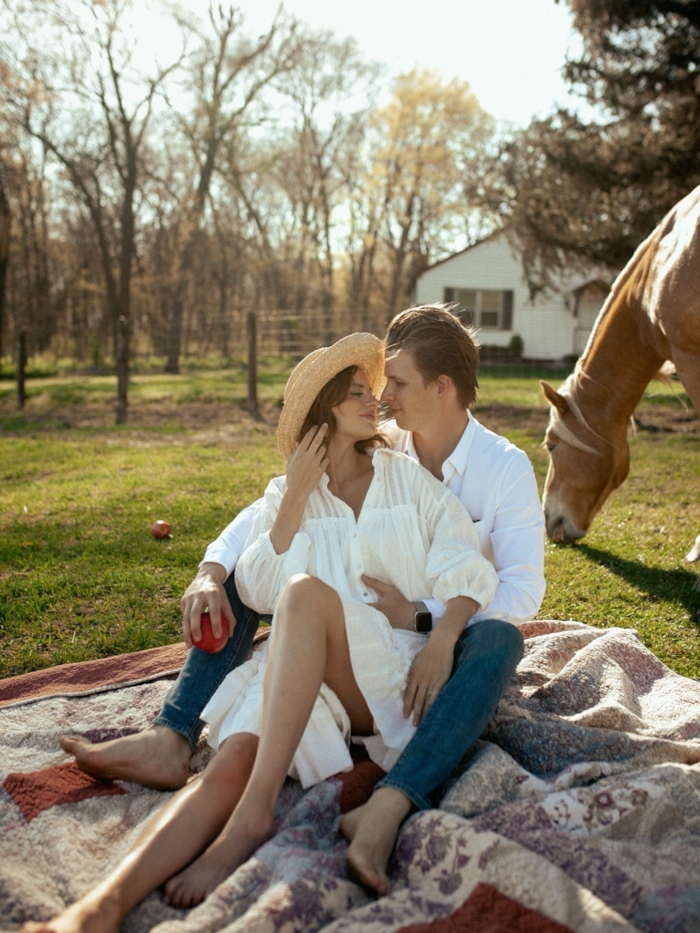 A couple picnics in a farm field with a horse nearby