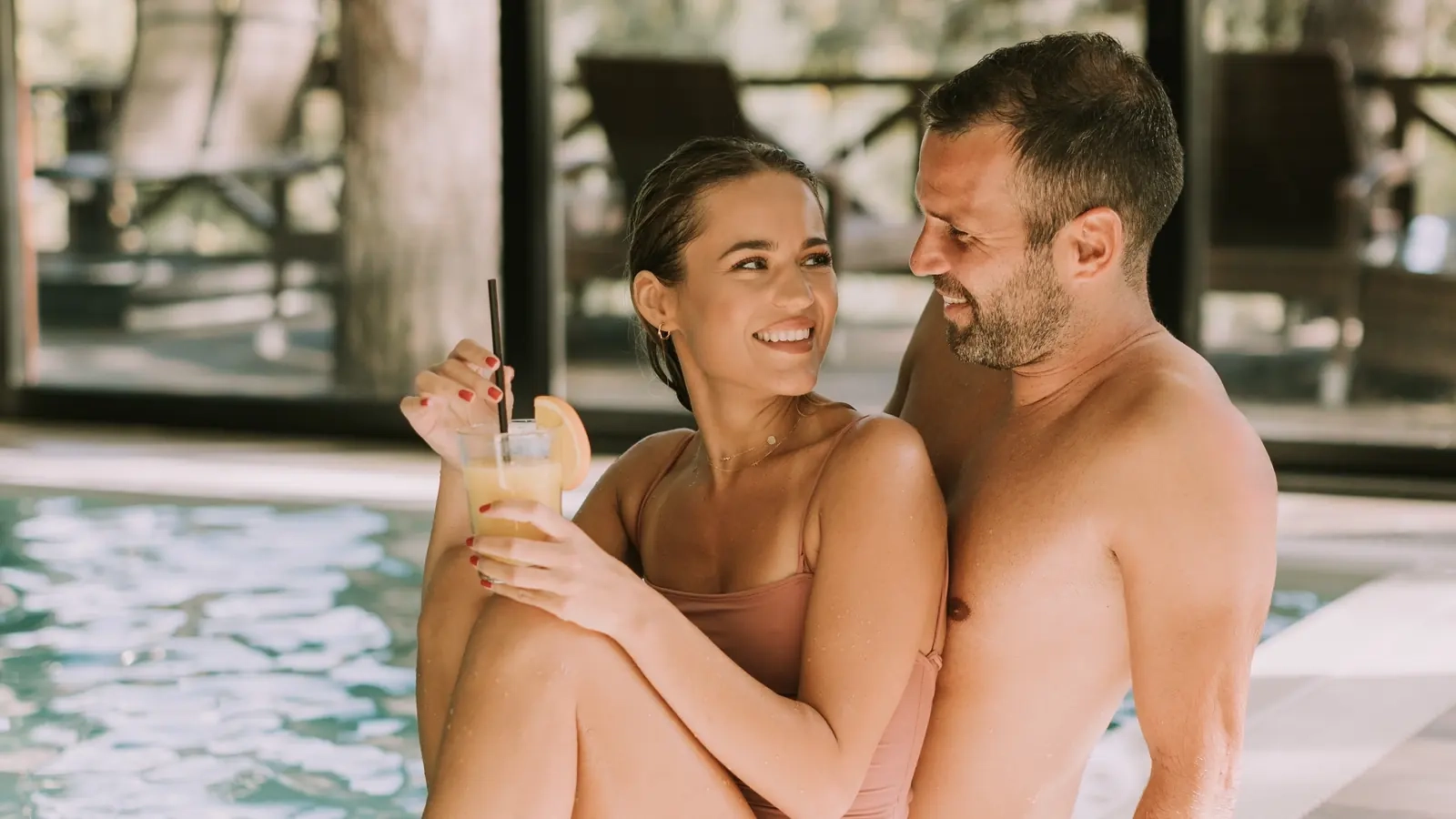 A laughing couple sitting together on the edge of an indoor pool