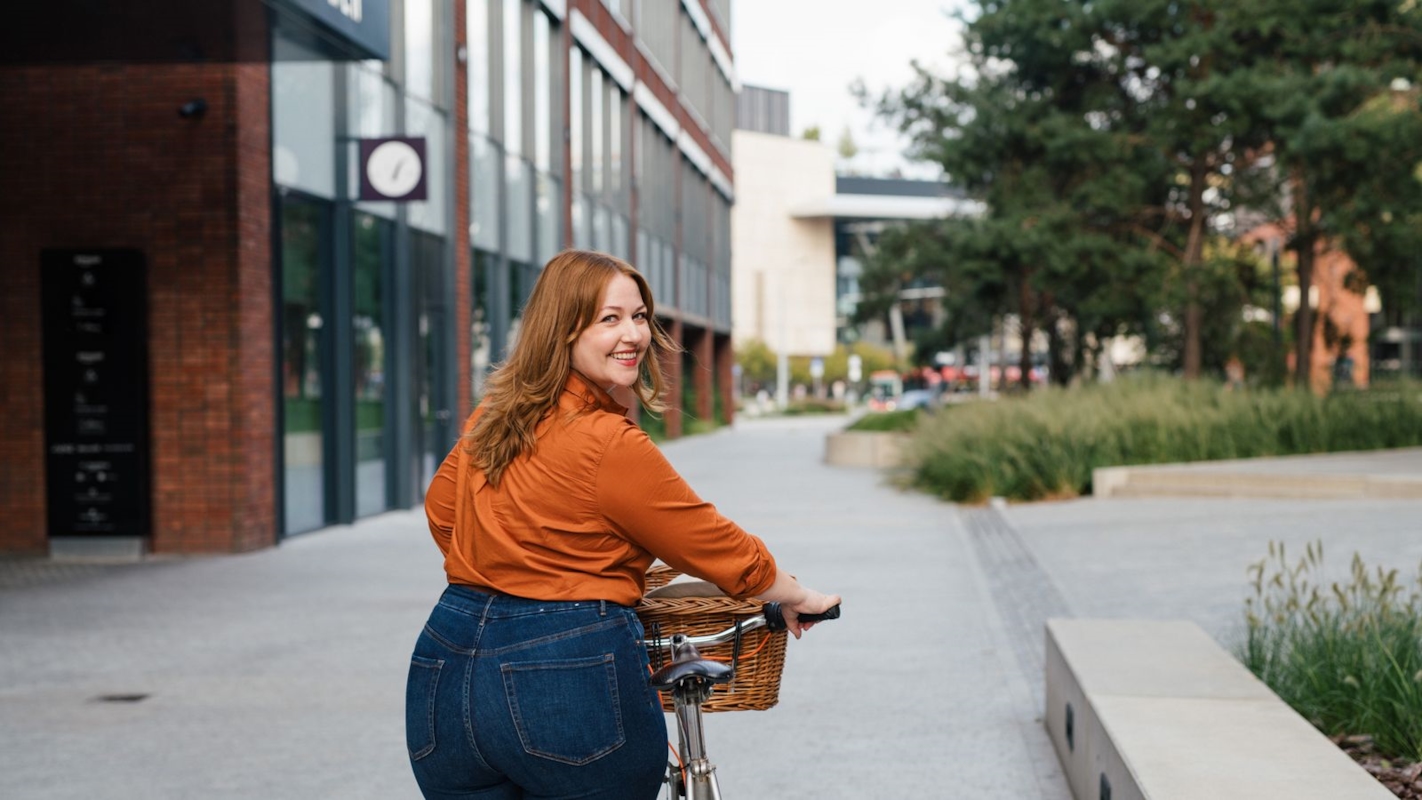 A woman walking her bike through a city plaza, looking back and smiling