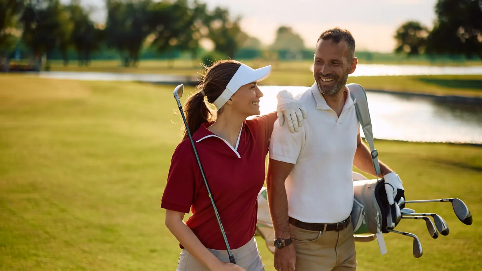 A smiling couple in their forties walking a sunny golf course with a bag of clubs