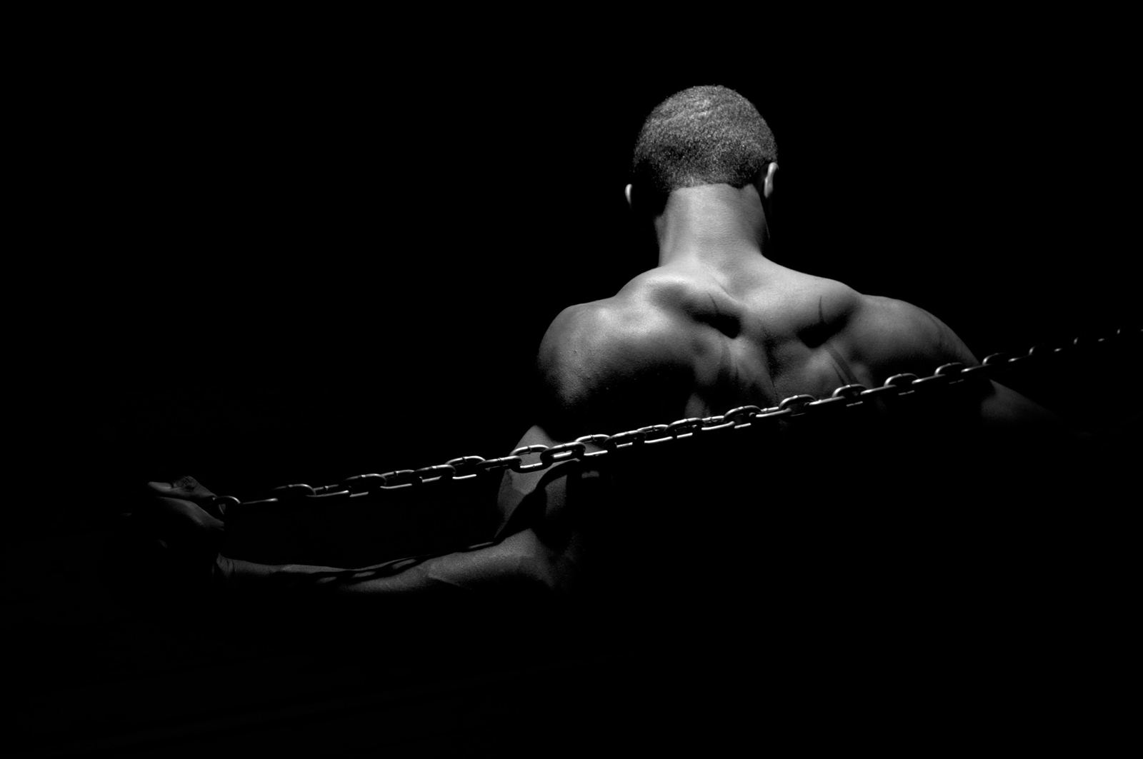 Muscular man in chains against a dark background