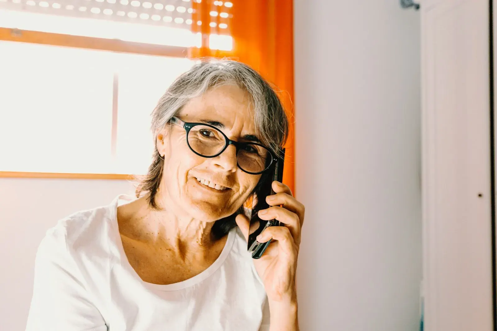A smiling woman in glasses on a phone call, looking knowingly at the camera