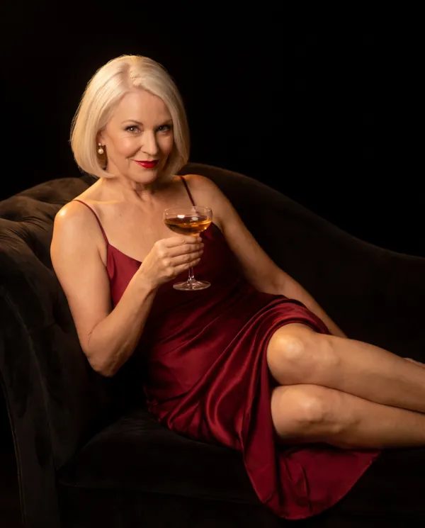 A glamorous blonde woman in her sixties in red satin with champagne