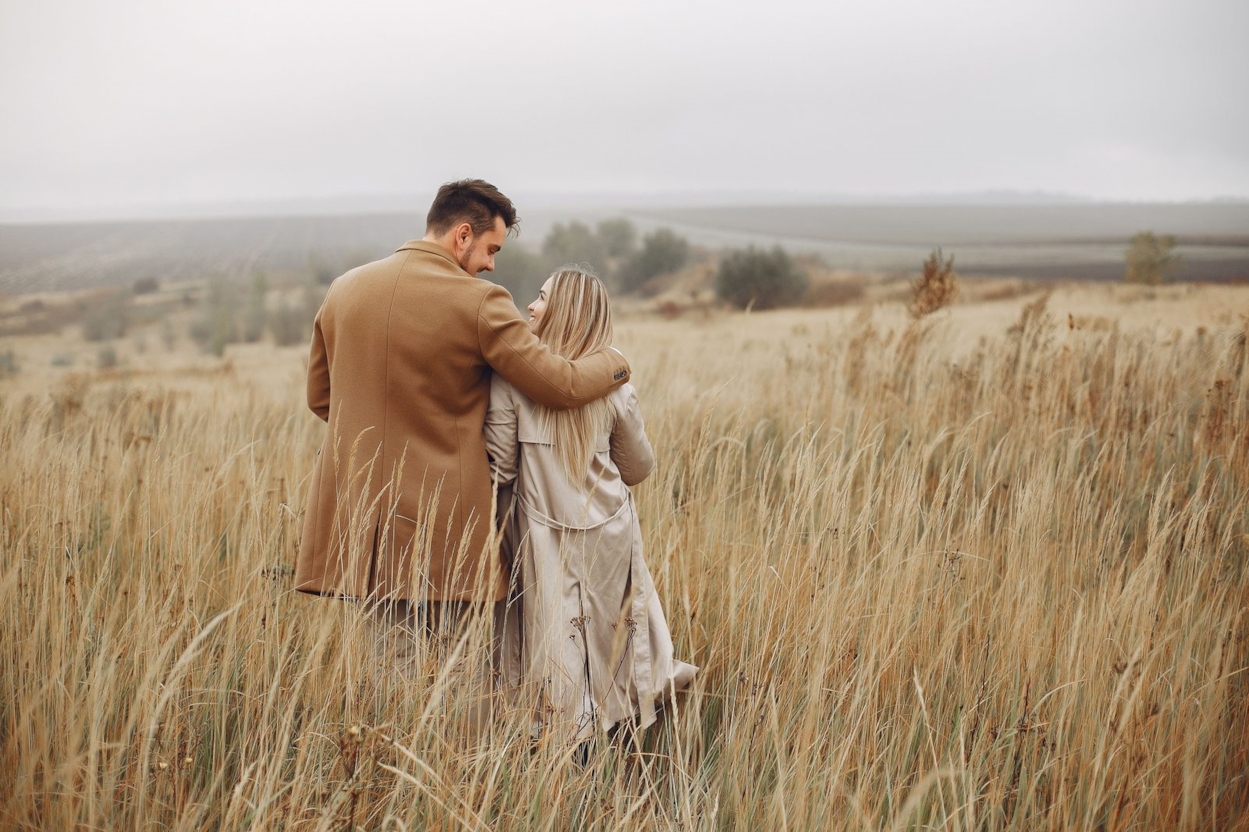 Couple in coats standing together in a field of tall grass