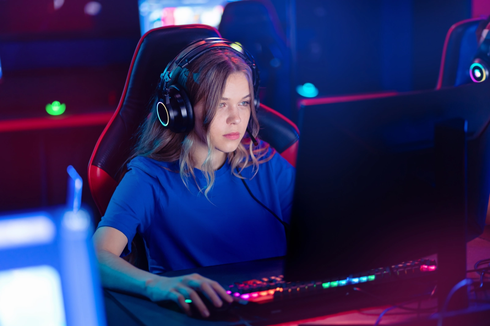 A woman in a headset playing at a PC with a glowing keyboard