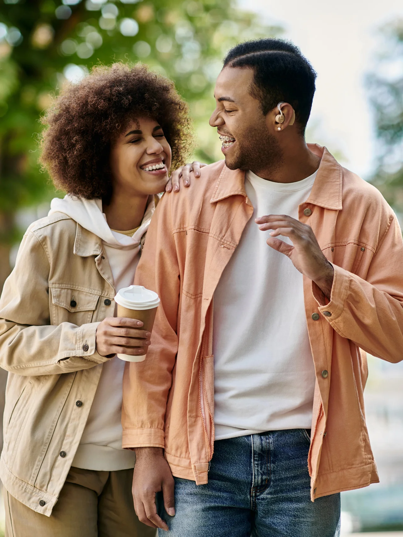 A laughing couple walking together in a park, holding a coffee