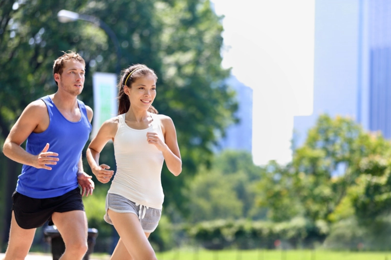 A man and woman running together through a sunny city park