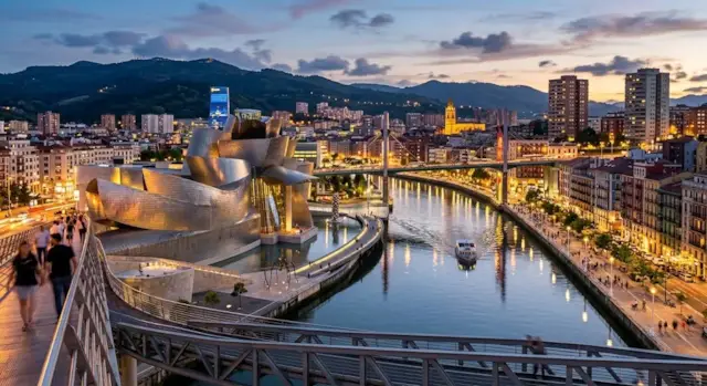 Museo Guggenheim y la ría de Bilbao al atardecer, con gente paseando por la pasarela