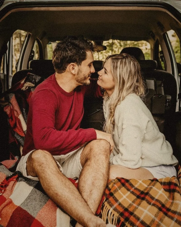 Couple sitting in the open boot of a car with a blanket