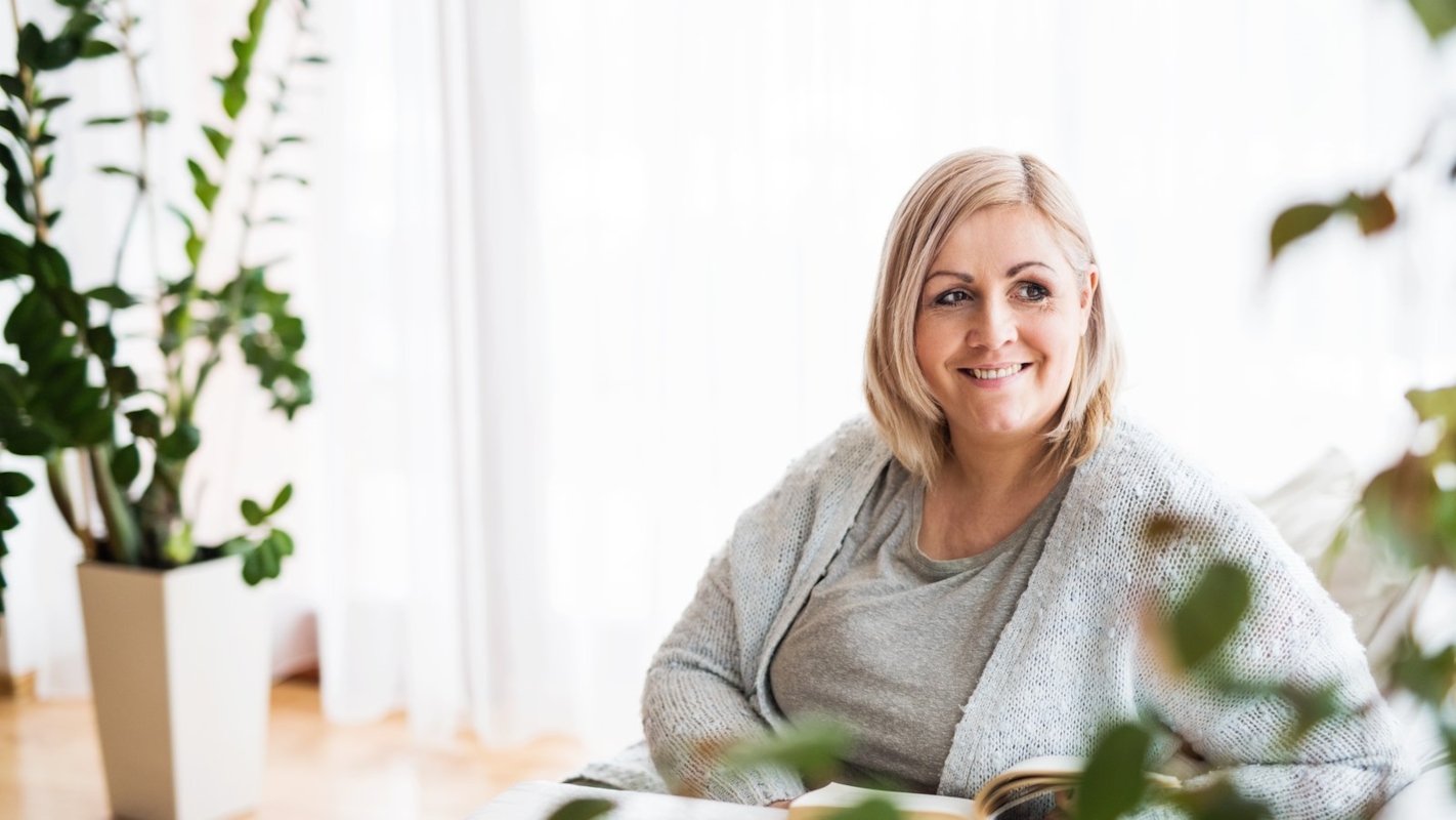 A woman relaxing at home with a book, smiling thoughtfully