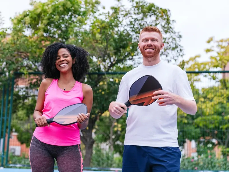 A smiling man and woman holding pickleball paddles on an outdoor court