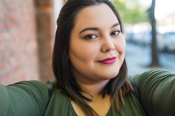 A curvy woman with dark hair and red lipstick smiling as she takes a selfie