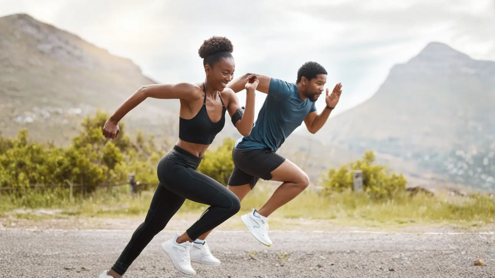 A smiling woman and man sprinting side by side along a mountain road