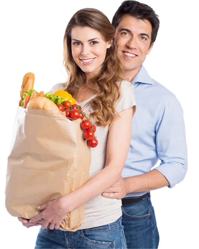 A smiling couple, she holding a paper bag of bread, peppers and tomatoes