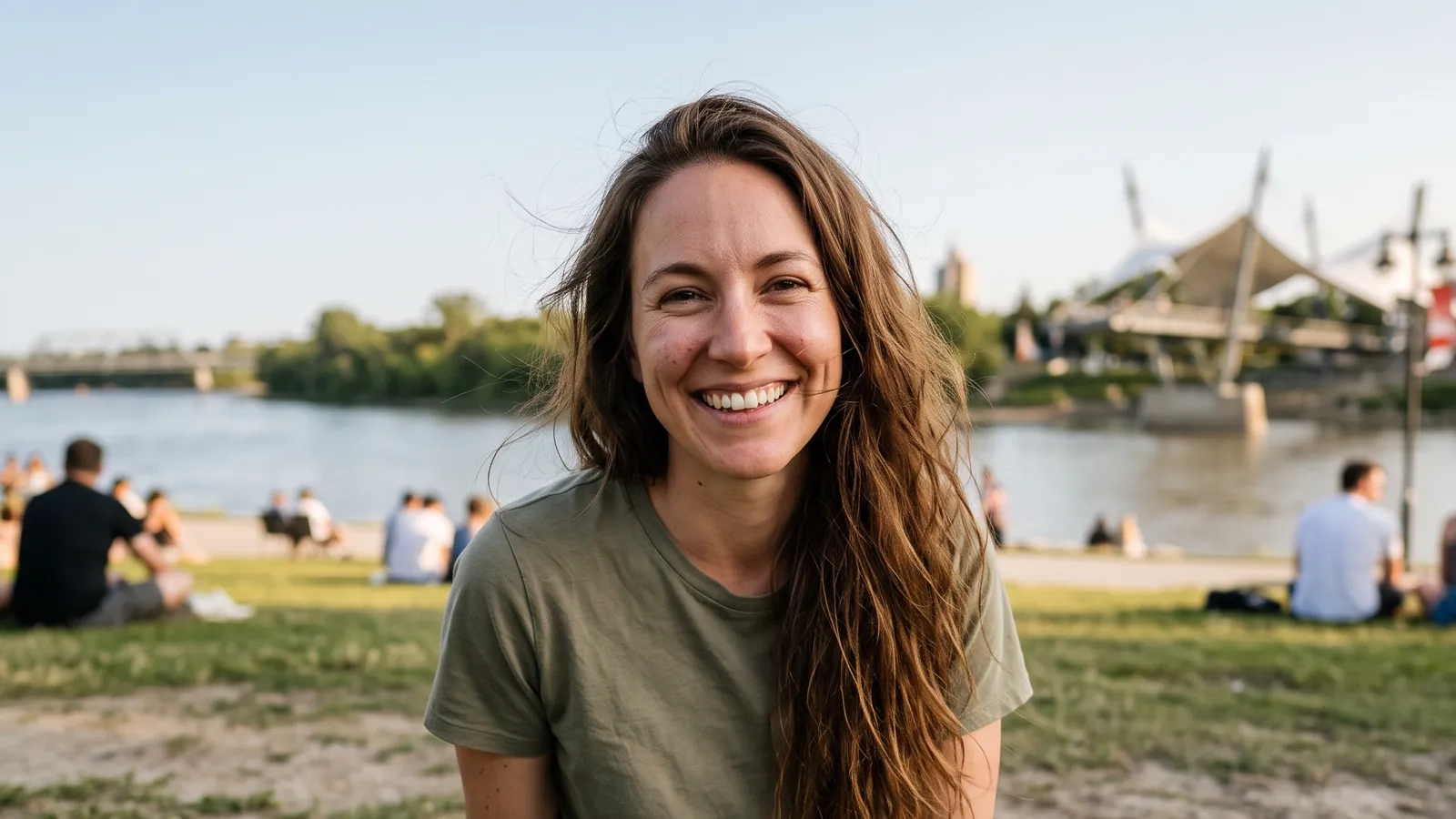 A smiling woman sitting on the riverside grass at The Forks in Winnipeg on a summer evening (AI-generated image)