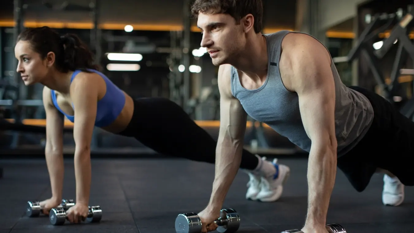 A man and woman doing dumbbell plank rows side by side in a gym