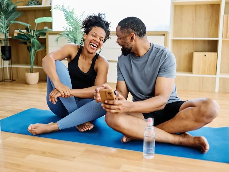 A relaxed couple laughing together on a yoga mat at home