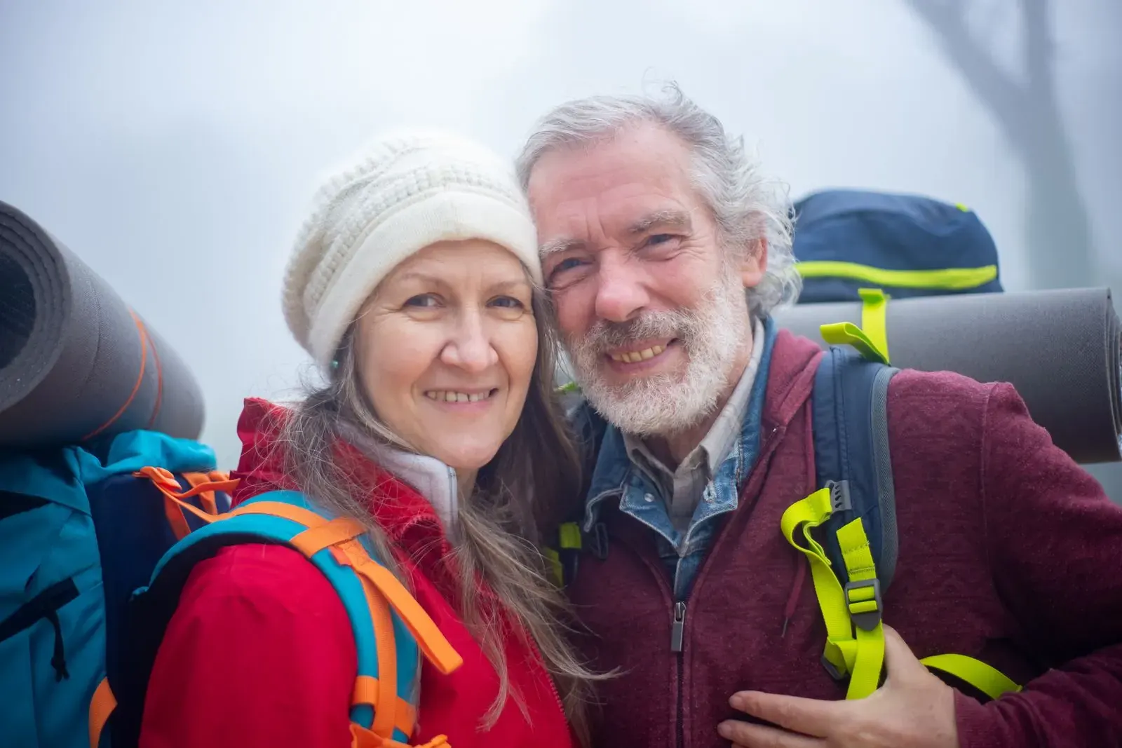 A smiling couple in hiking gear and woolly hats taking a selfie outdoors