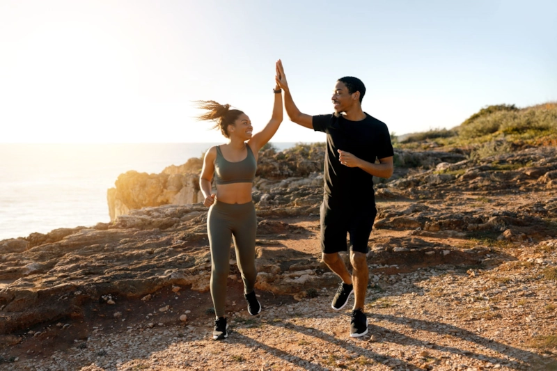 A woman and man high-fiving on a clifftop trail by the sea