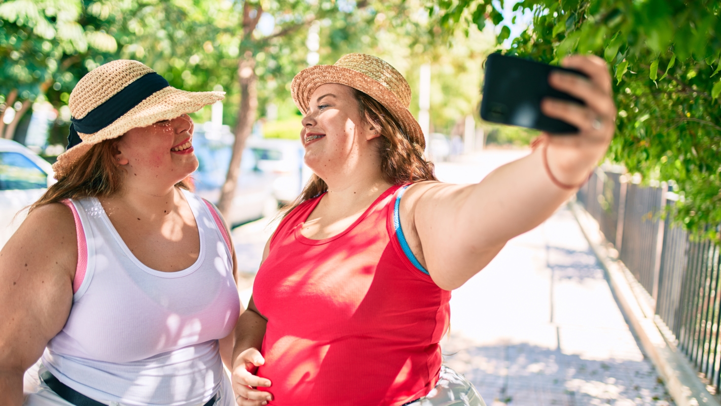 Two friends taking a selfie together outdoors, laughing