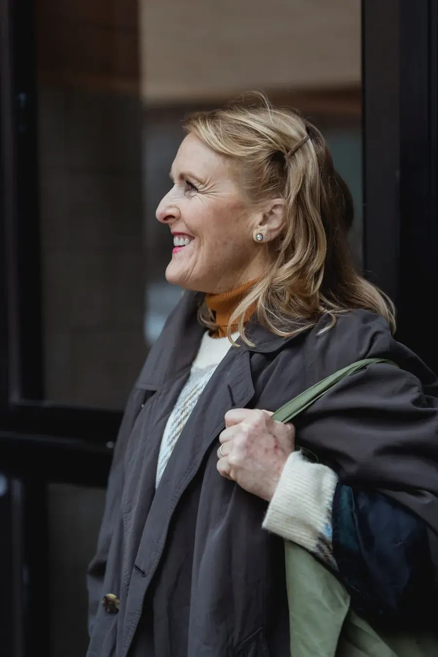 A smiling woman in a winter coat heading out of the door
