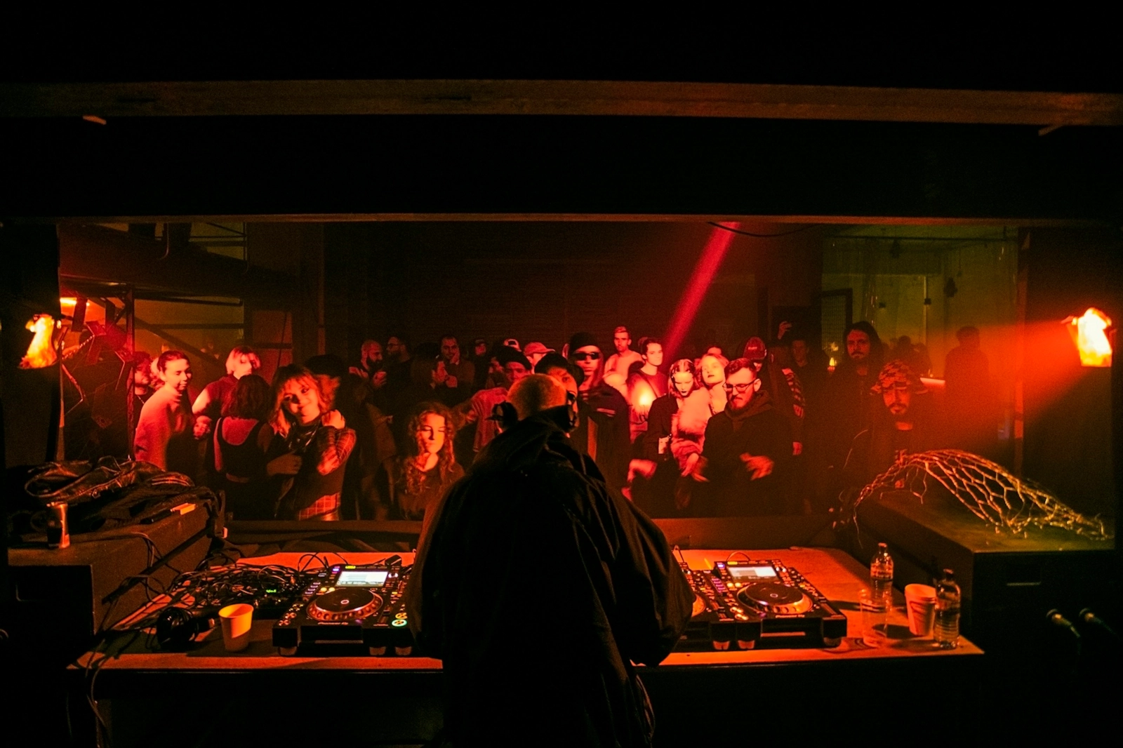 A DJ at the decks in front of a packed, red-lit room