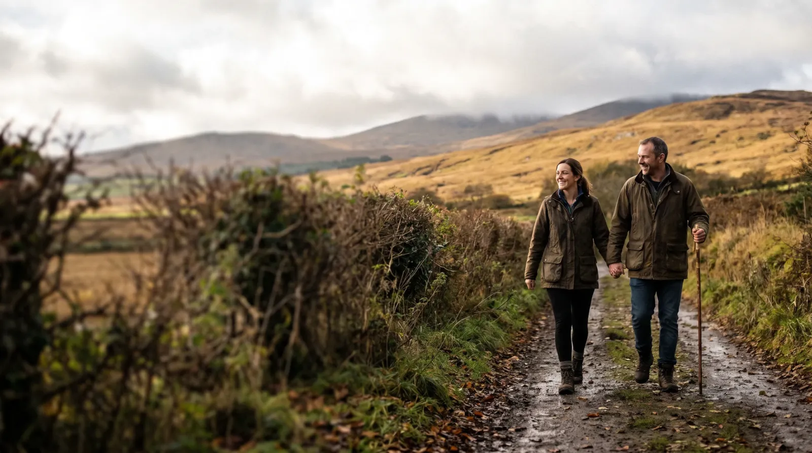 A couple holding hands on a country path below the Sperrin Mountains; the man walks with a stick