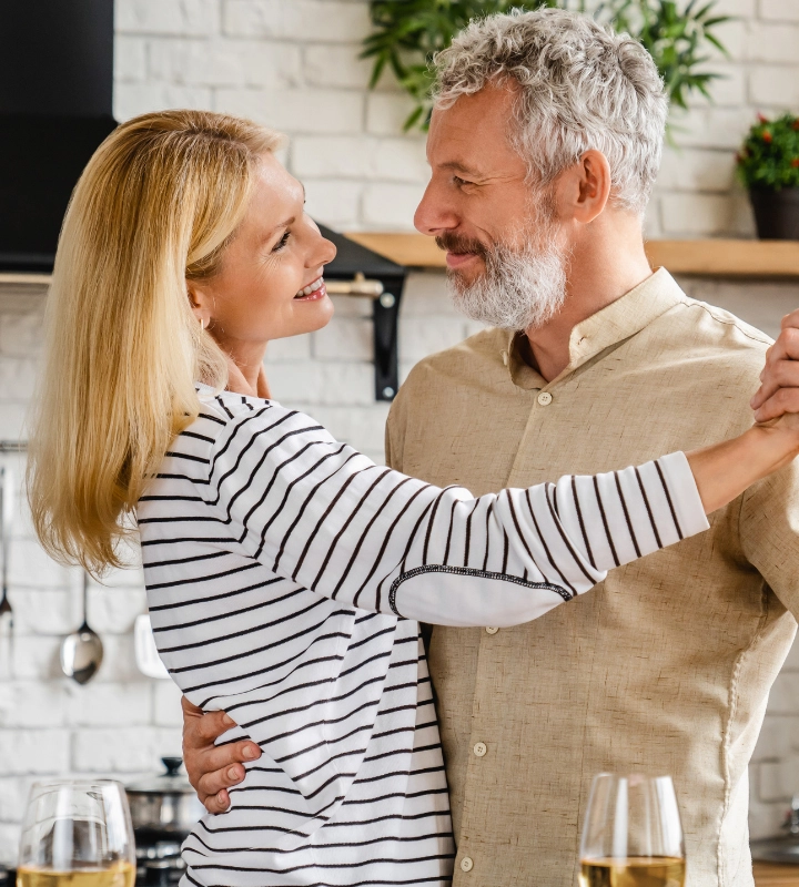 A couple dancing together in a kitchen with glasses of wine