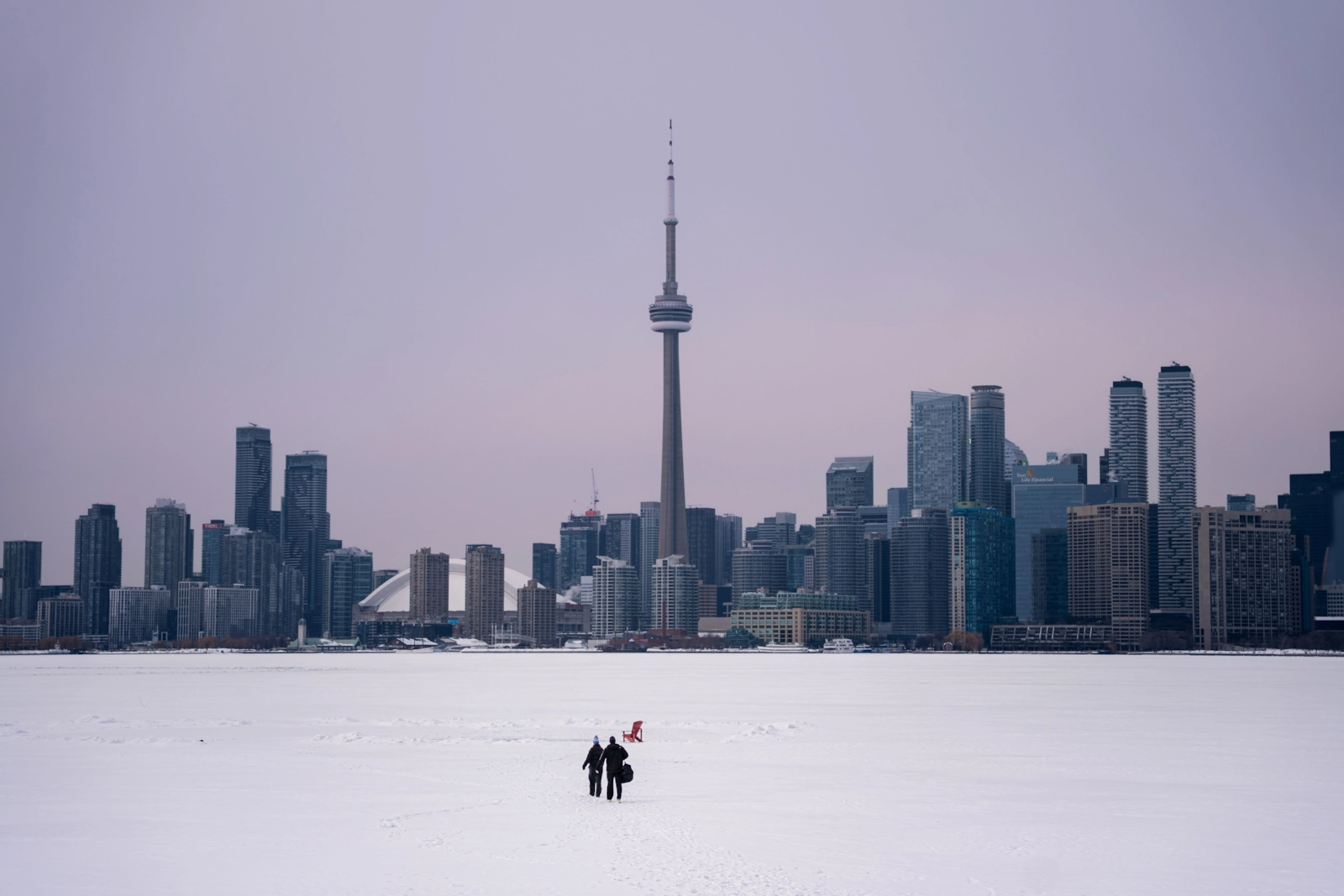 Two people walking across a snowy field with a city skyline behind them