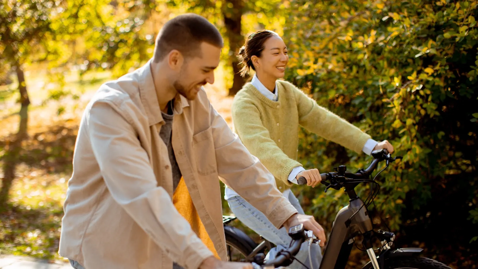 A smiling couple riding bikes together along a sunny autumn woodland trail