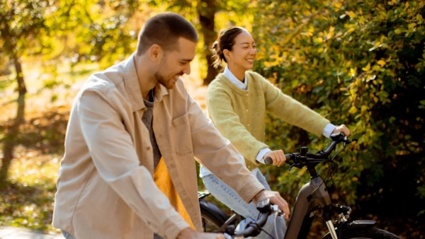 A smiling couple riding bikes together along a sunny autumn woodland trail