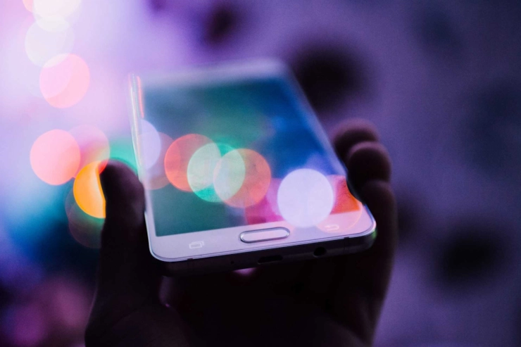 A hand holding a smartphone, its screen reflecting blurred coloured lights