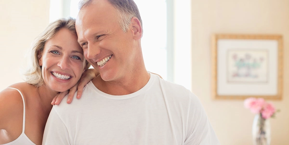 A smiling couple in their fifties, her arm resting on his shoulder