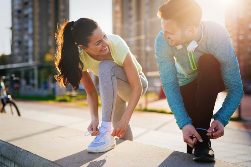 A smiling woman and man tying their running shoes in the city