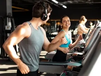 A man and woman smiling at each other while running on neighboring treadmills