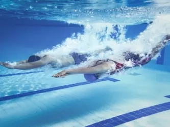 Two swimmers diving into a pool, seen underwater above the lane markings