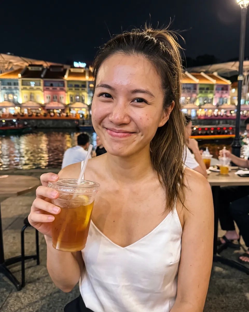 A woman with a high ponytail and a white satin camisole smiles on the riverside promenade at Clarke Quay at night, lit shophouses behind her (AI-generated image)